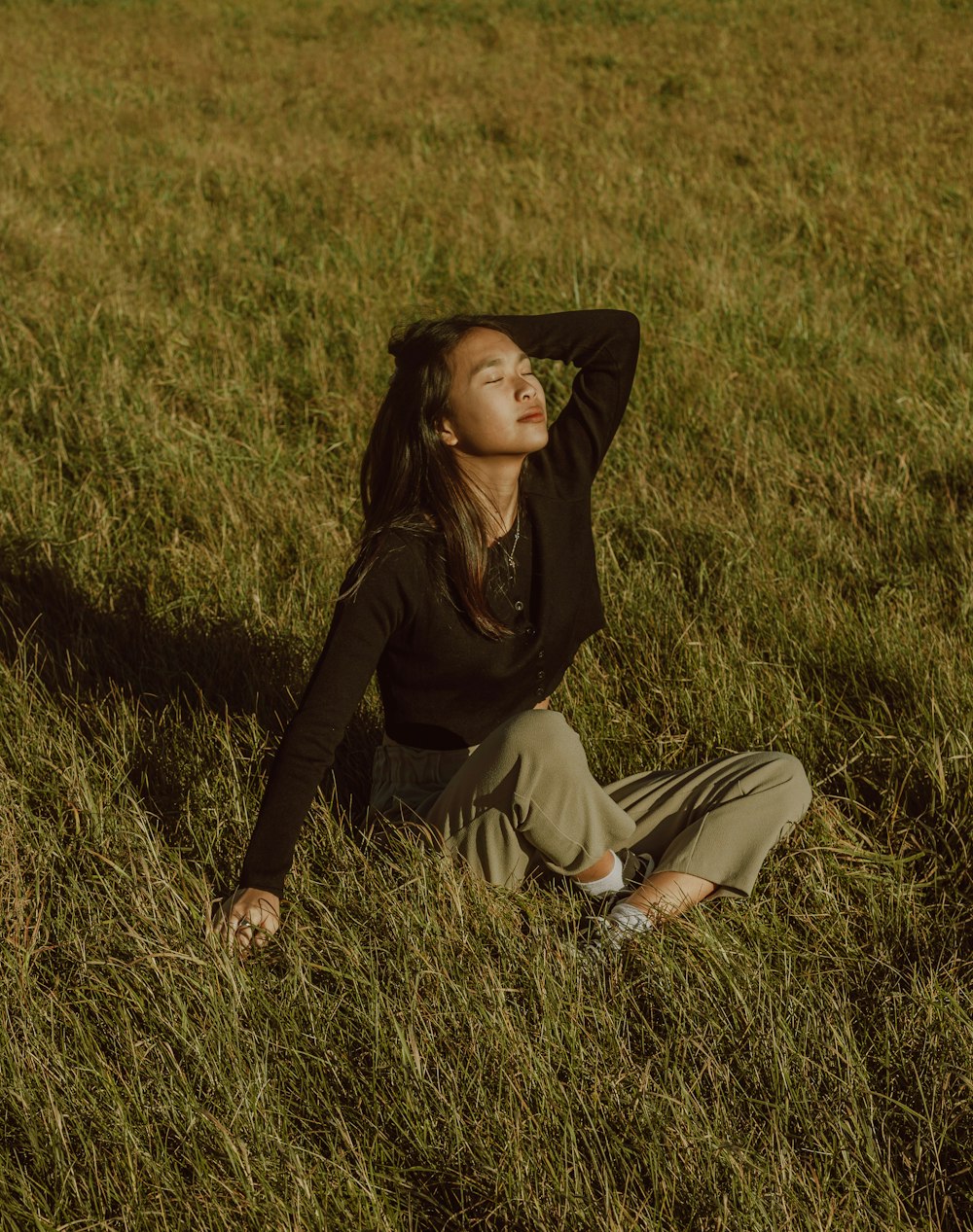 woman in black long sleeve shirt and brown pants sitting on green grass field during daytime