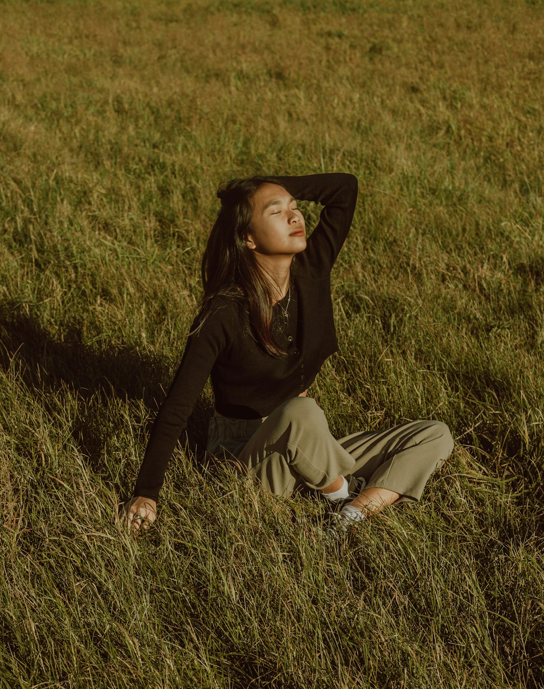 woman in black long sleeve shirt and brown pants sitting on green grass field during daytime