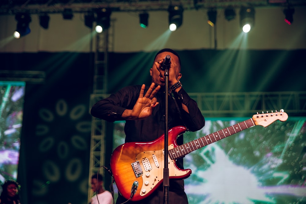 man in black jacket playing brown electric guitar