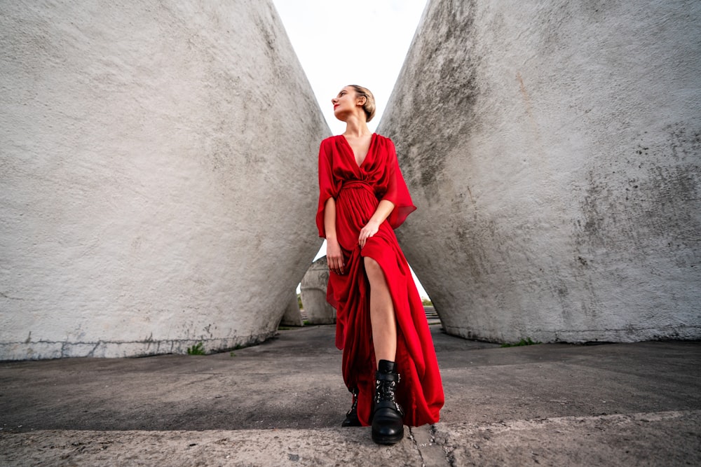 donna in abito rosso a maniche lunghe e stivali neri in piedi accanto al muro di cemento grigio durante il giorno