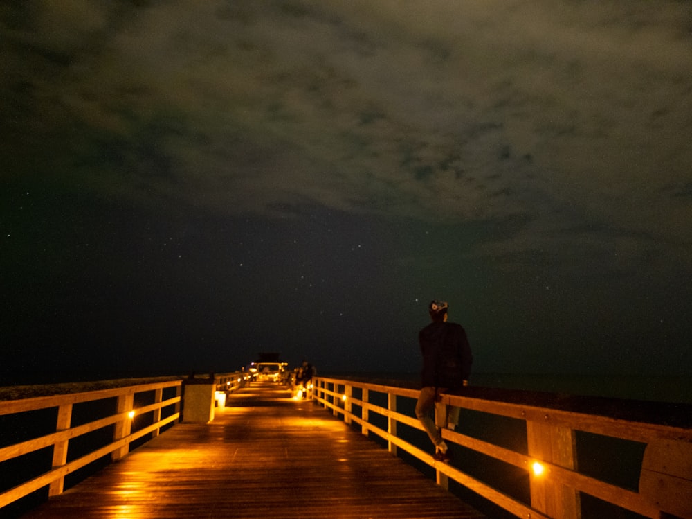 man in black jacket standing on brown wooden dock during night time