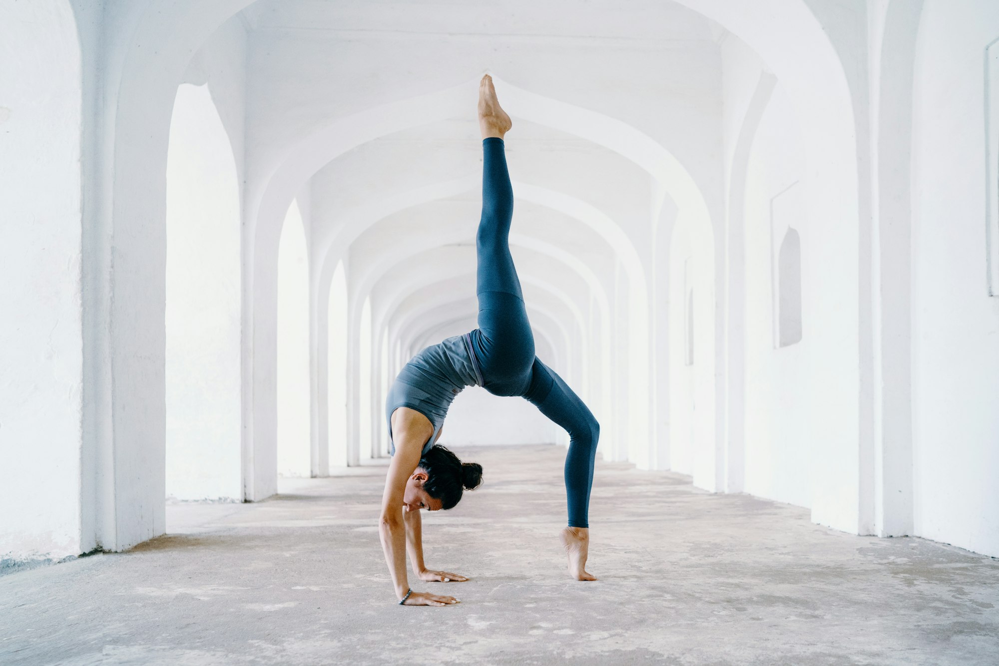 A flexible yogini doing a backbend pose in the middle of a white archway. Photo by Oksana Taran.