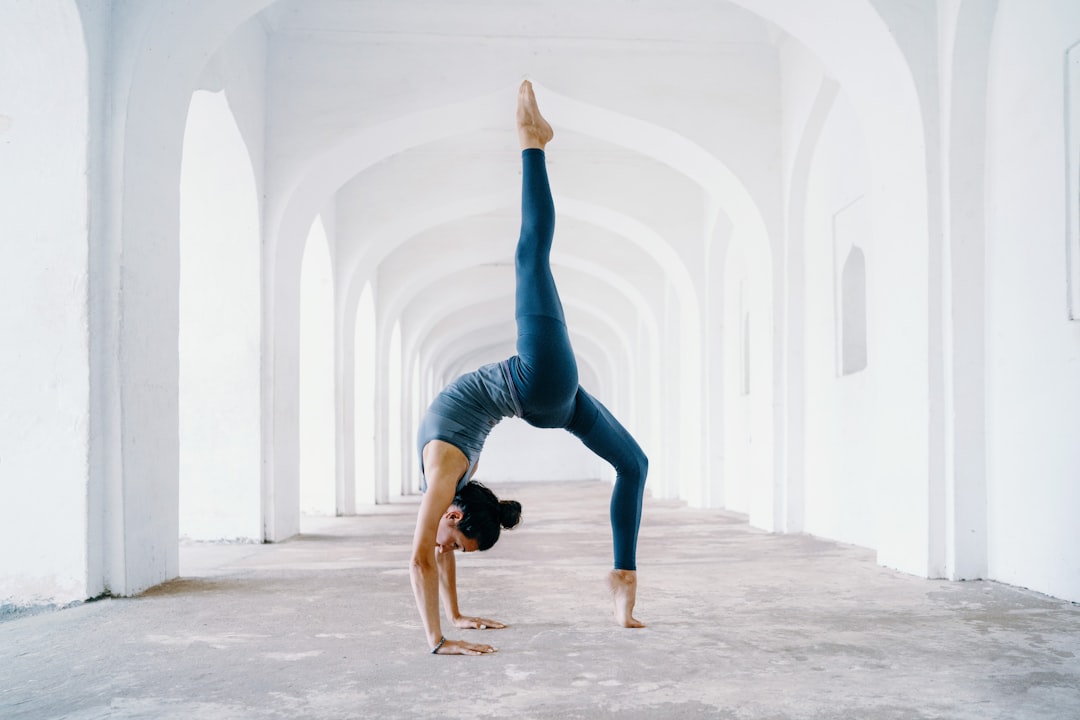 A flexible yogini doing a backbend pose in the middle of a white archway. Photo by Oksana Taran.