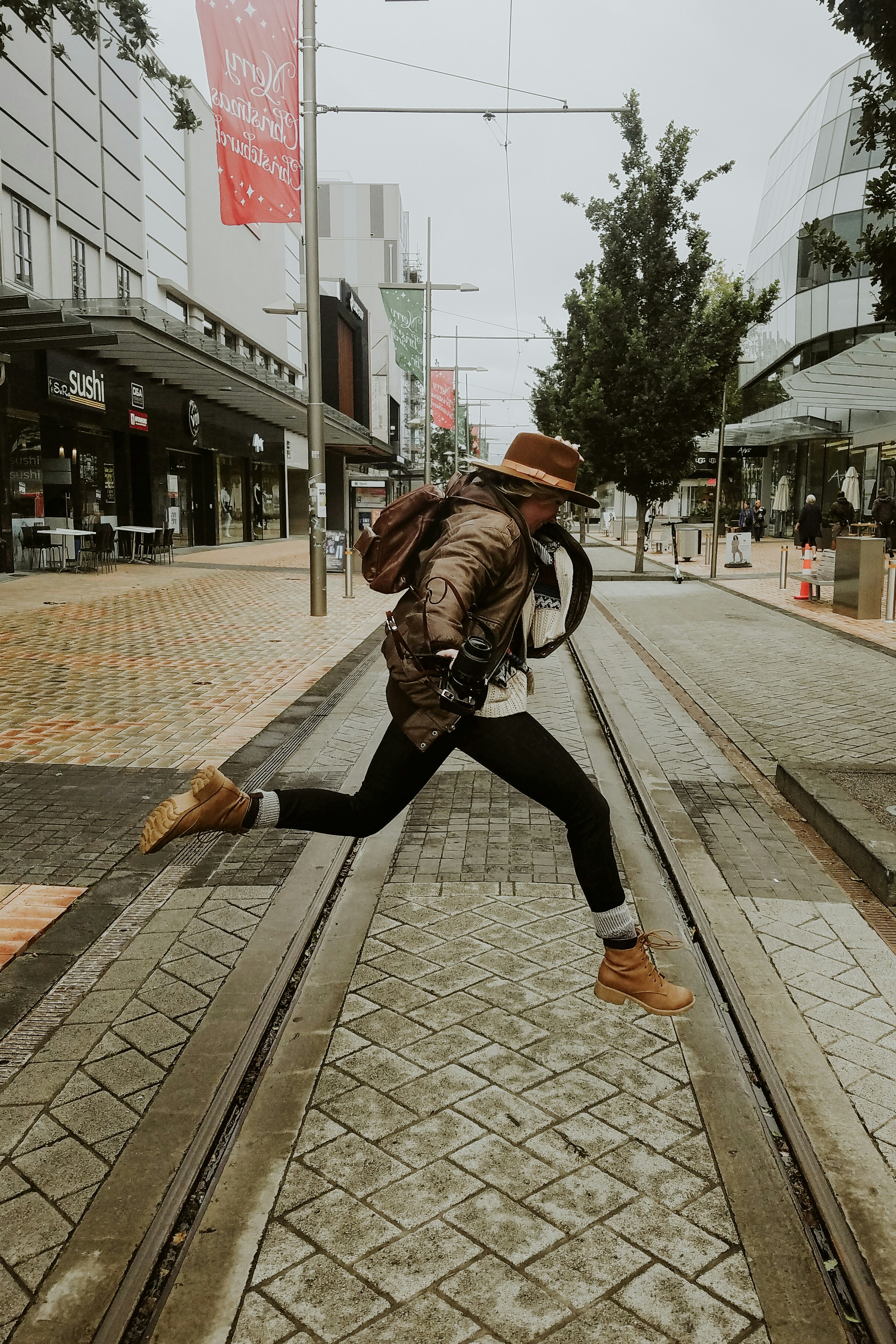 donna in giacca di pelle marrone e pantaloni neri che cammina sul marciapiede durante il giorno