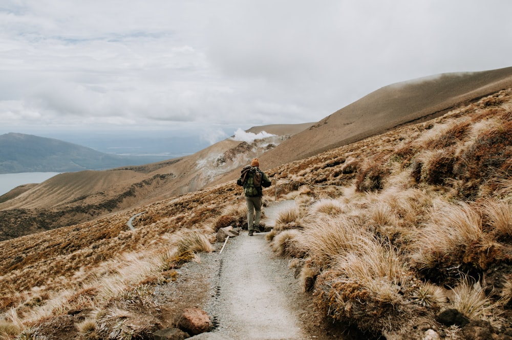 people walking on pathway near brown mountain under white clouds during daytime