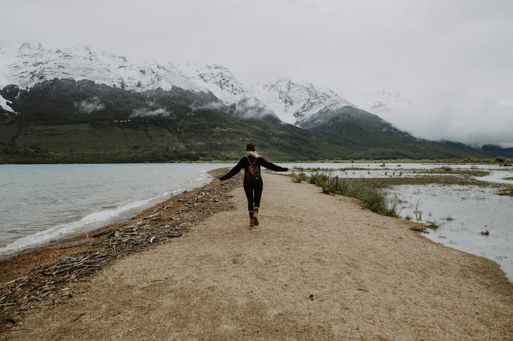 woman in black long sleeve shirt and black pants walking on brown dirt road near lake