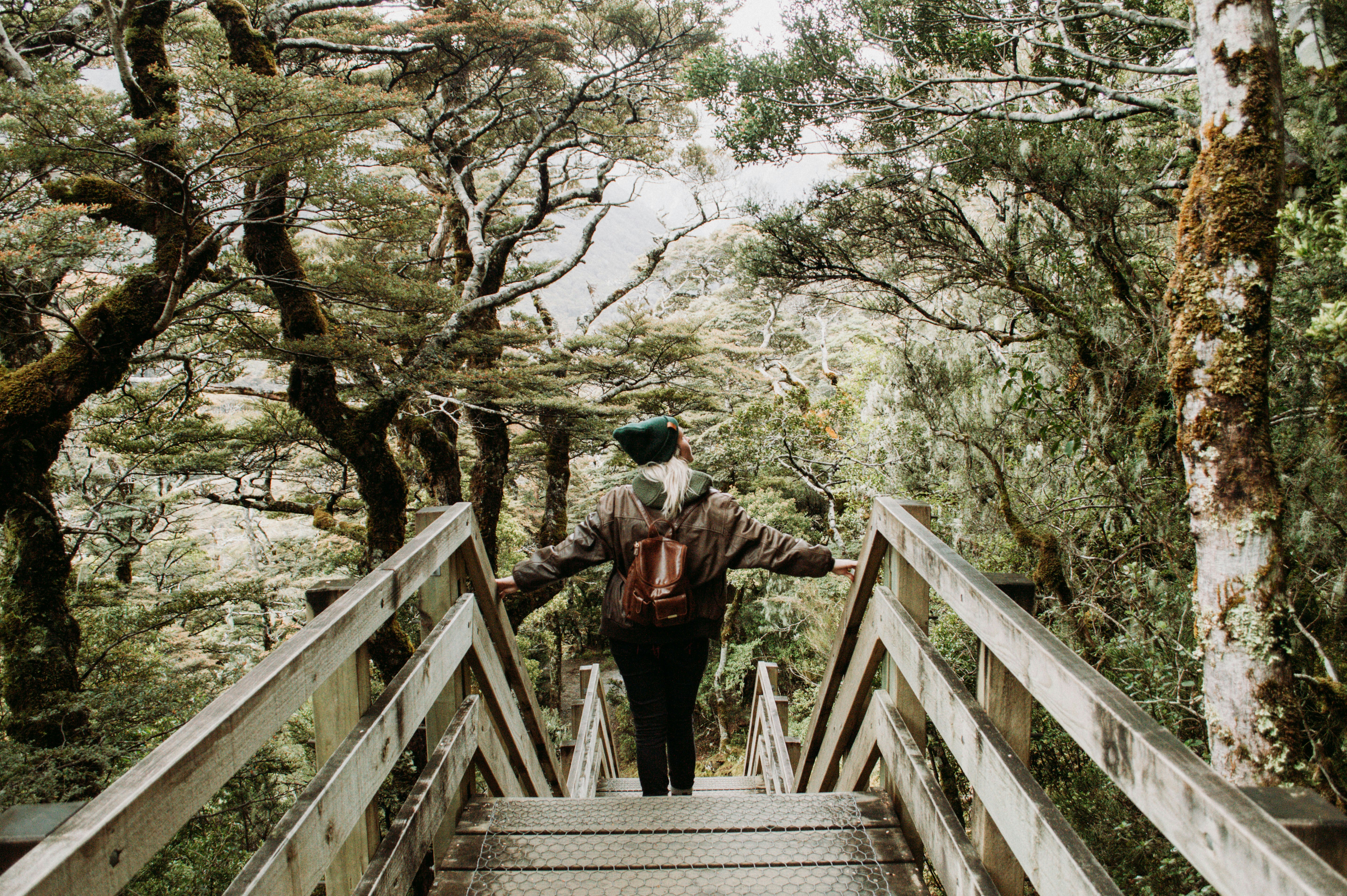uomo in giacca nera e pantaloni neri che cammina sul ponte di legno