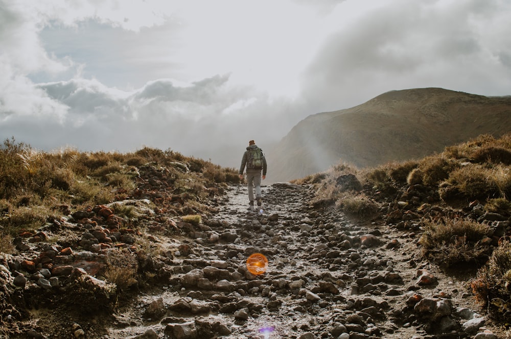 person in white shirt walking on rocky road during daytime