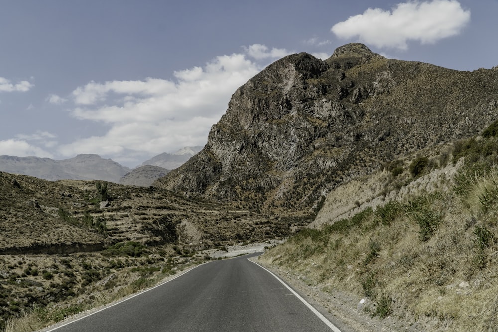 gray asphalt road near brown mountain under blue sky during daytime