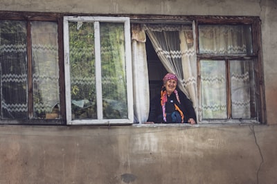 woman in black jacket standing near white wooden framed glass window log home teams background