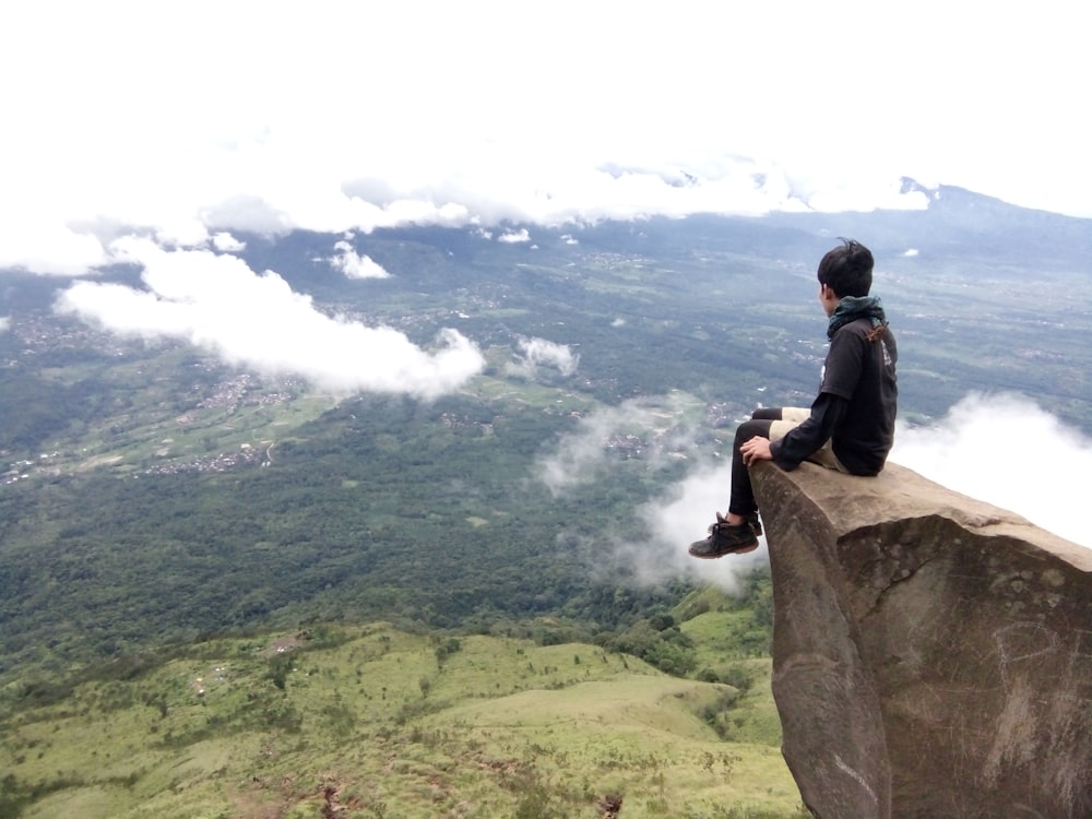 man in black jacket sitting on rock formation during daytime