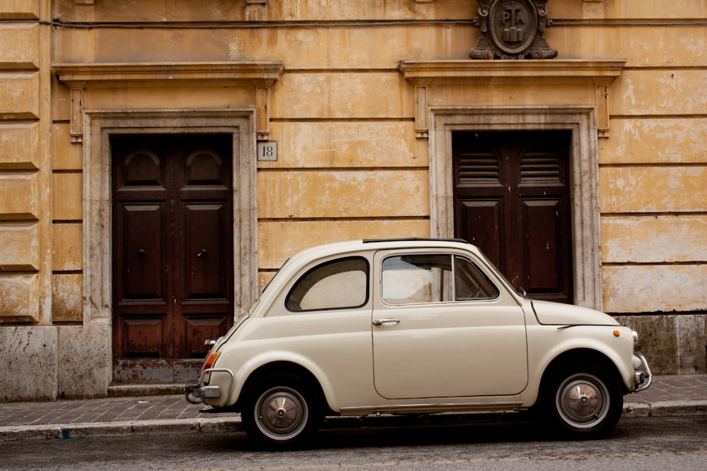 white volkswagen beetle parked beside brown brick building during daytime