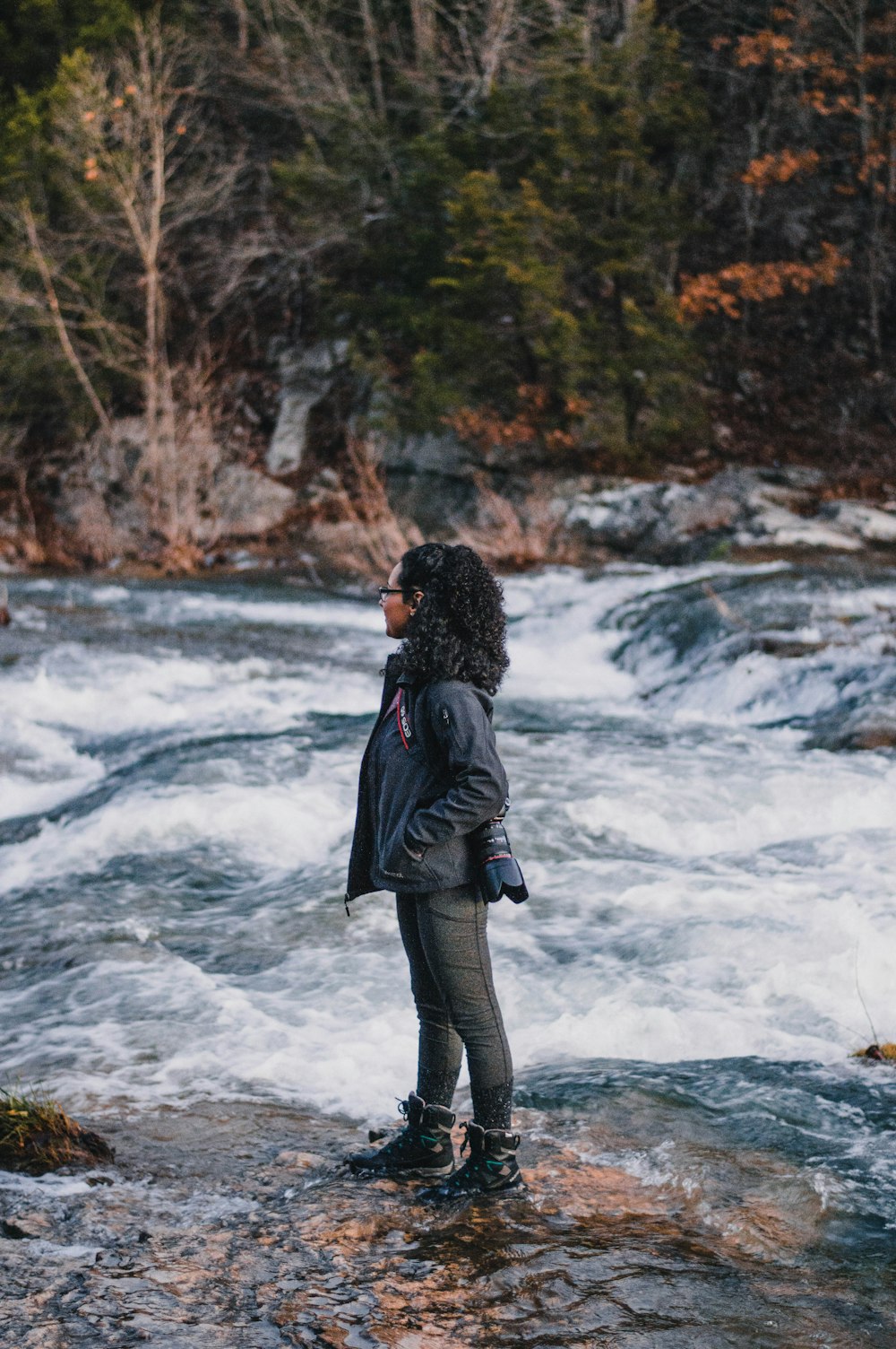 mulher na jaqueta preta de pé no rio durante o dia