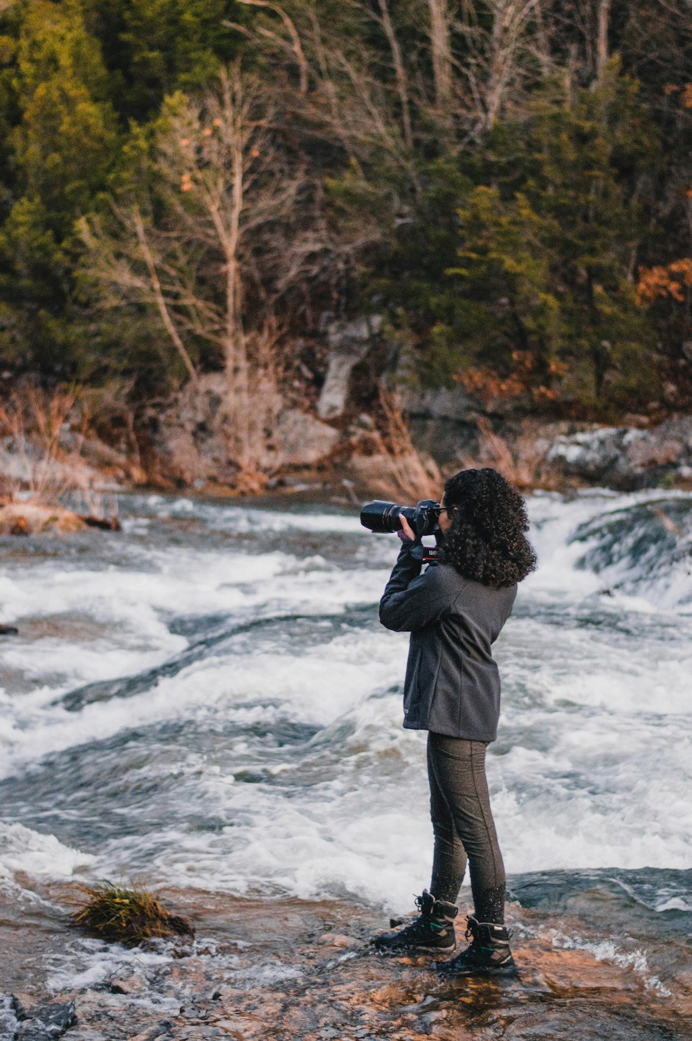 man in black jacket and gray pants standing on rocky shore during daytime