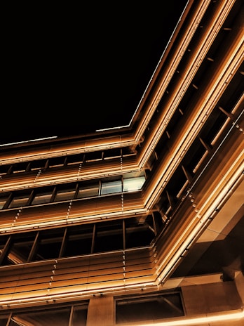 A modern architectural structure with sleek lines and illuminated windows featuring warm lighting against a dark night sky.