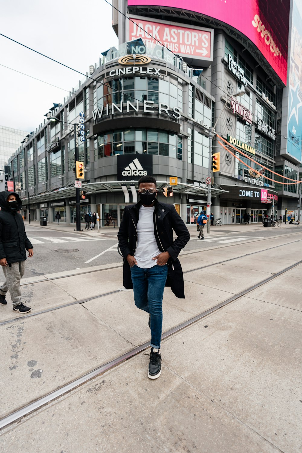 man in black jacket and blue denim jeans walking on sidewalk during daytime