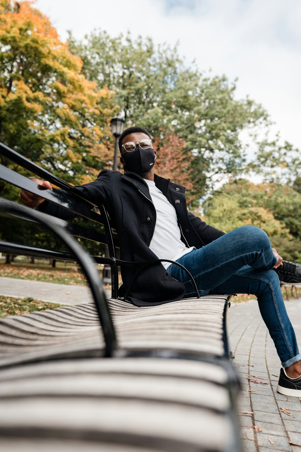 uomo in giacca nera e jeans blu in denim seduto sulla panca di metallo nero durante il giorno
