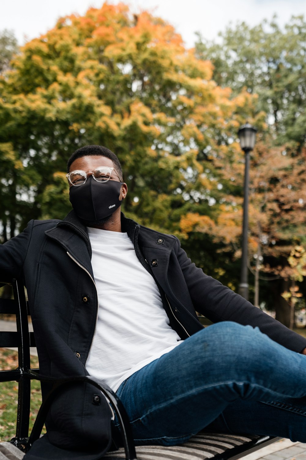 man in black jacket and blue denim jeans wearing black sunglasses sitting on black metal bench