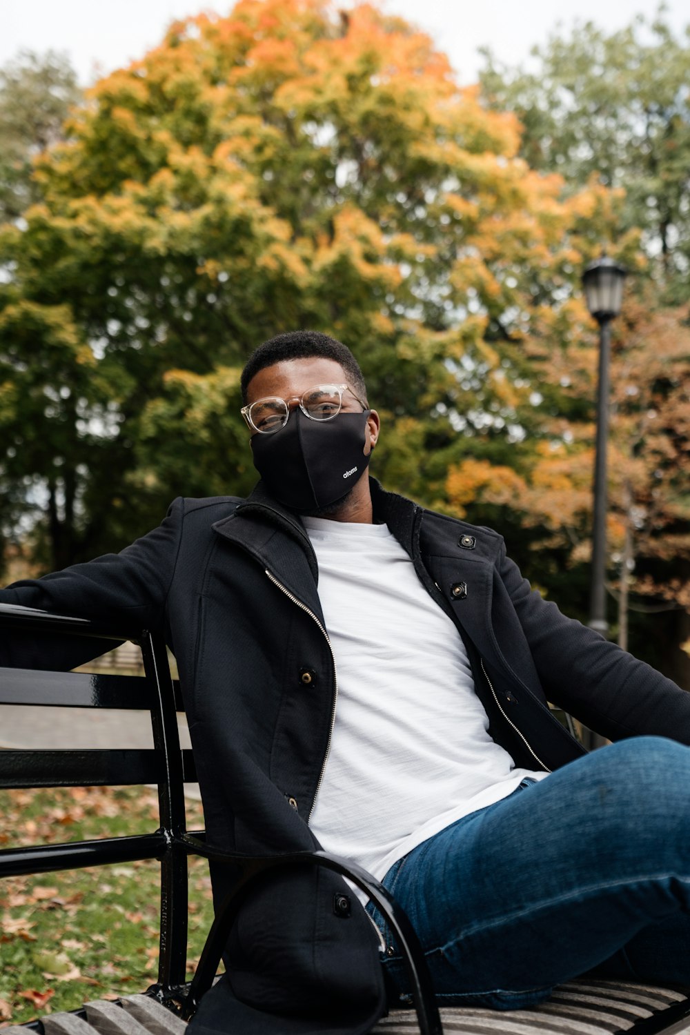 man in black jacket and blue denim jeans sitting on bench during daytime