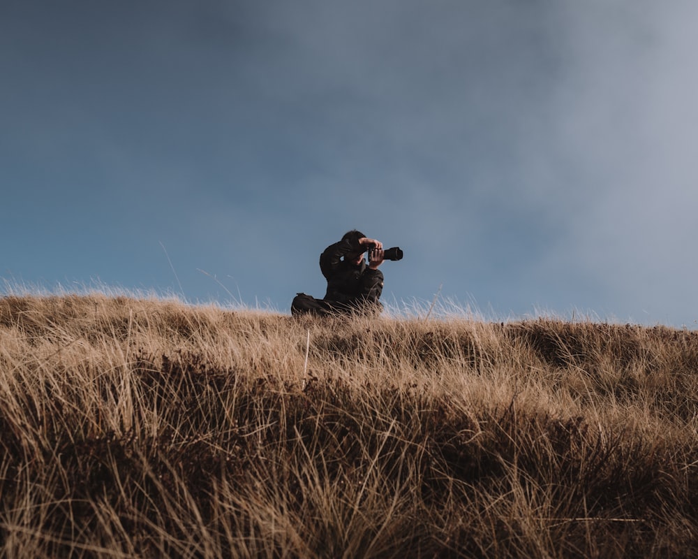 Cane nero di taglia media a pelo corto seduto sul campo di erba marrone sotto il cielo blu durante il giorno