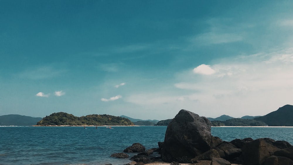 black rock formation on sea under blue sky during daytime