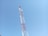 A tall communication tower with red and white metal structures extends upwards against a clear blue sky. Several antennas and satellite dishes are attached to the tower at various points.