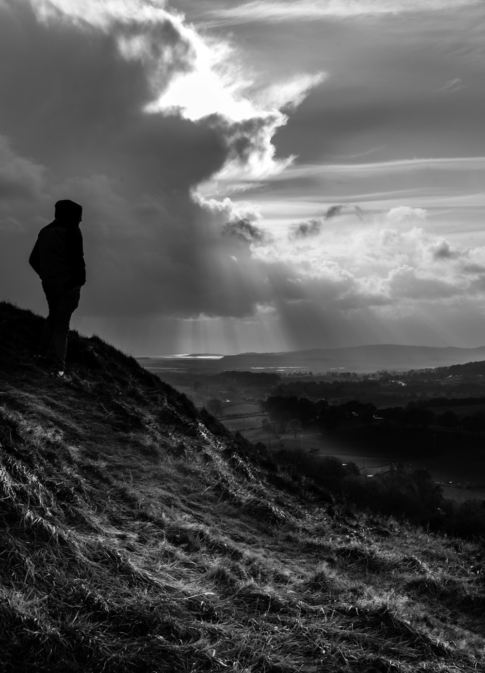 grayscale photo of man standing on rock formation