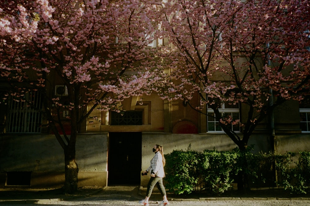 woman in white long sleeve shirt and white skirt standing under pink cherry blossom tree during