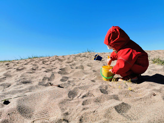 A joyful child playing with a colorful bucket and shovel on a sunny beach shore.