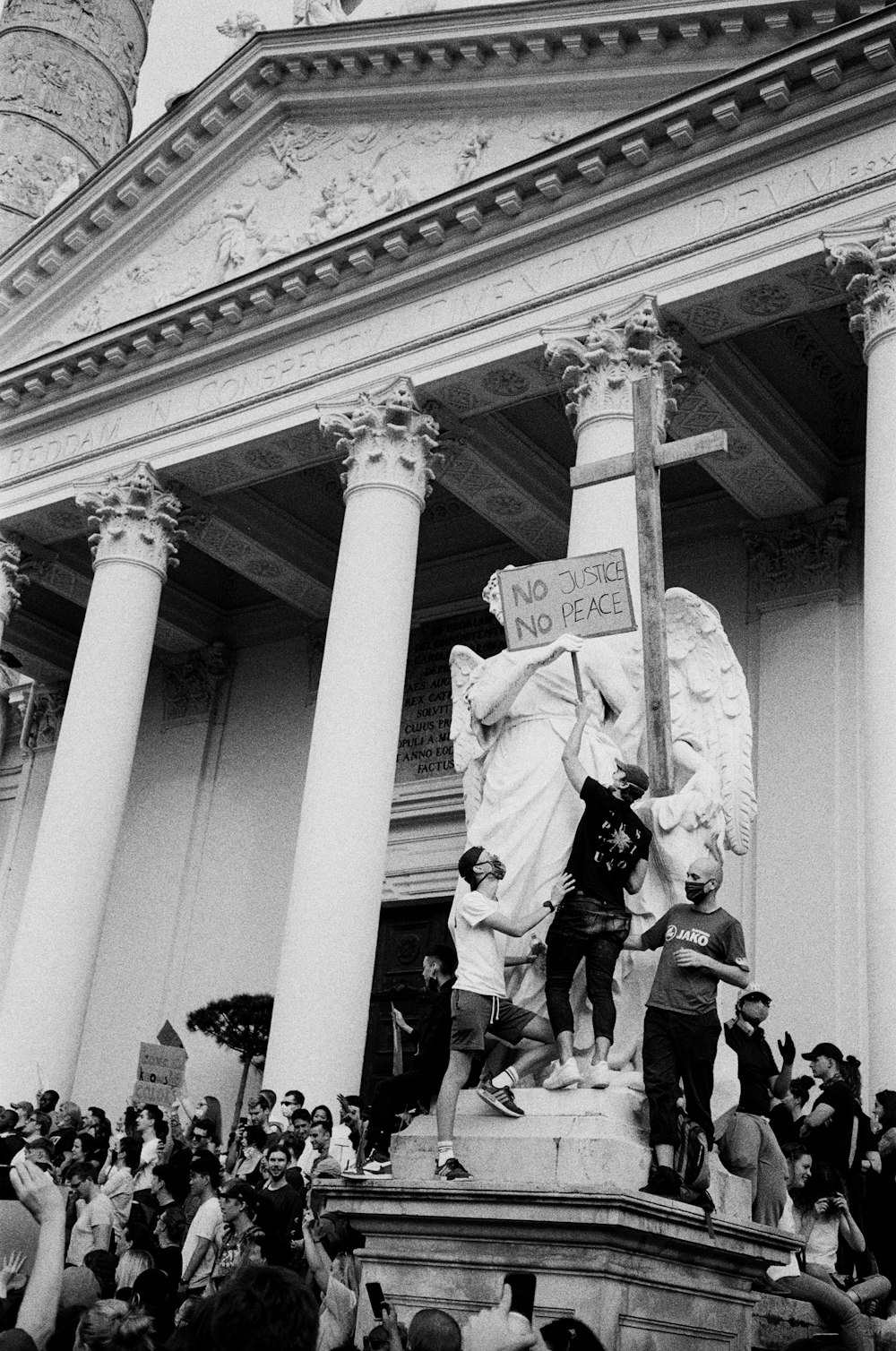 grayscale photo of man in jacket standing in front of statue