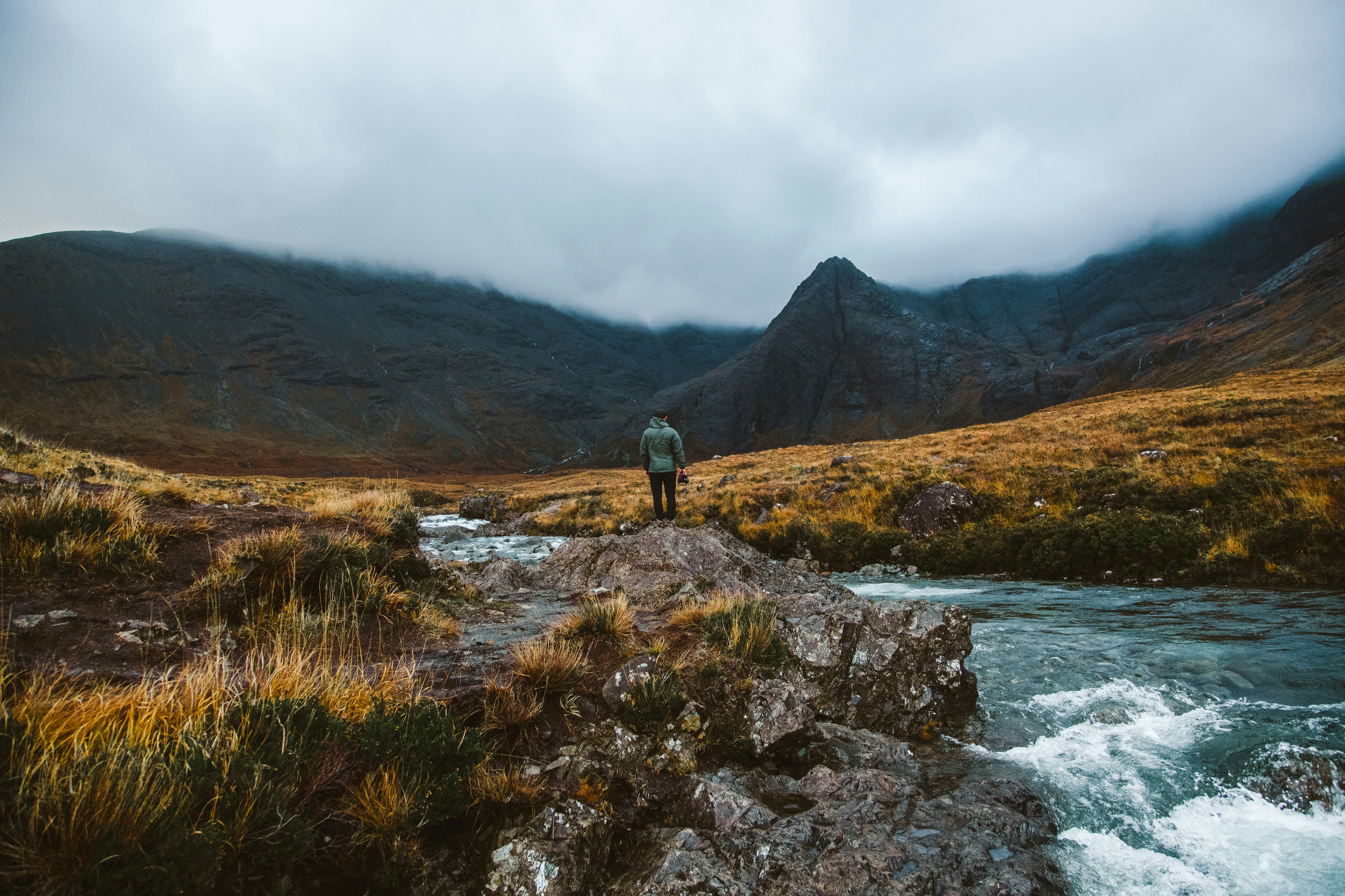 person in green jacket standing on brown grass field near body of water during daytime