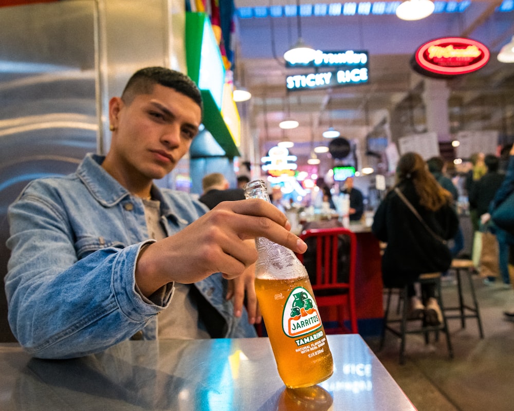 man in blue denim jacket holding orange juice