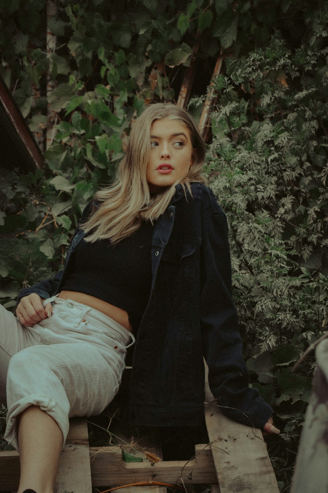 woman in black jacket and gray denim jeans sitting on brown wooden bench