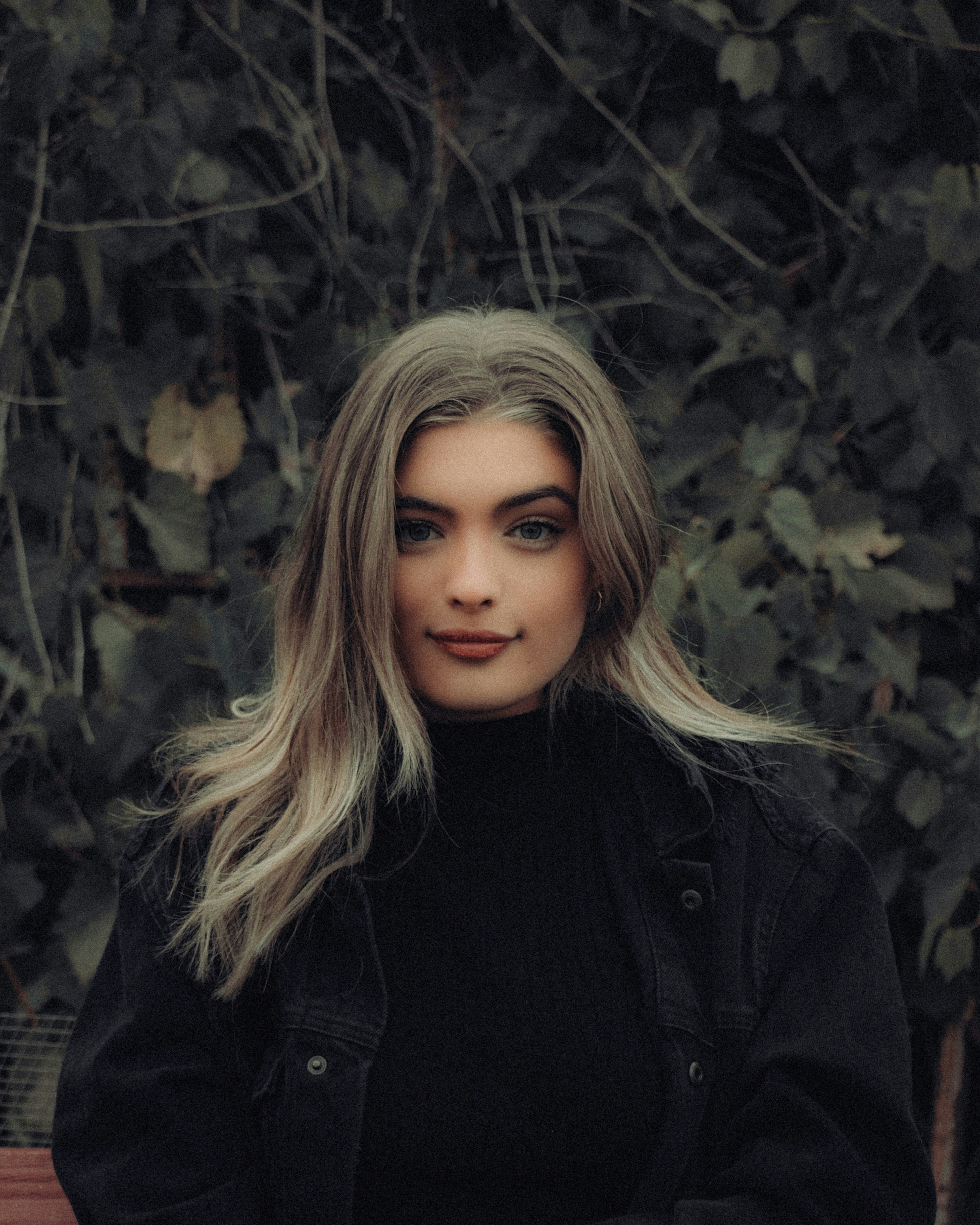 woman in black jacket standing near green leaves