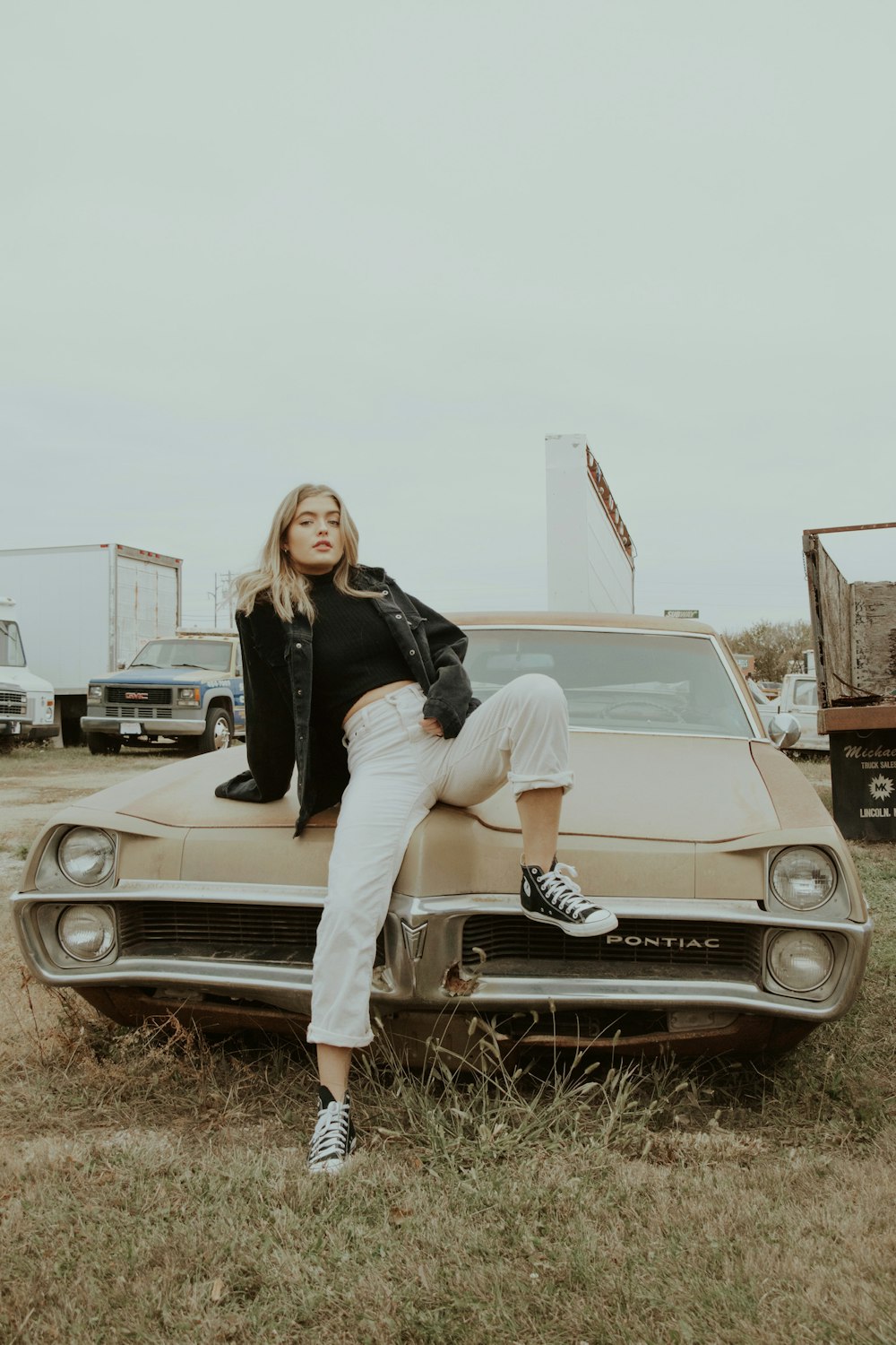 woman in black jacket and white pants sitting on white car