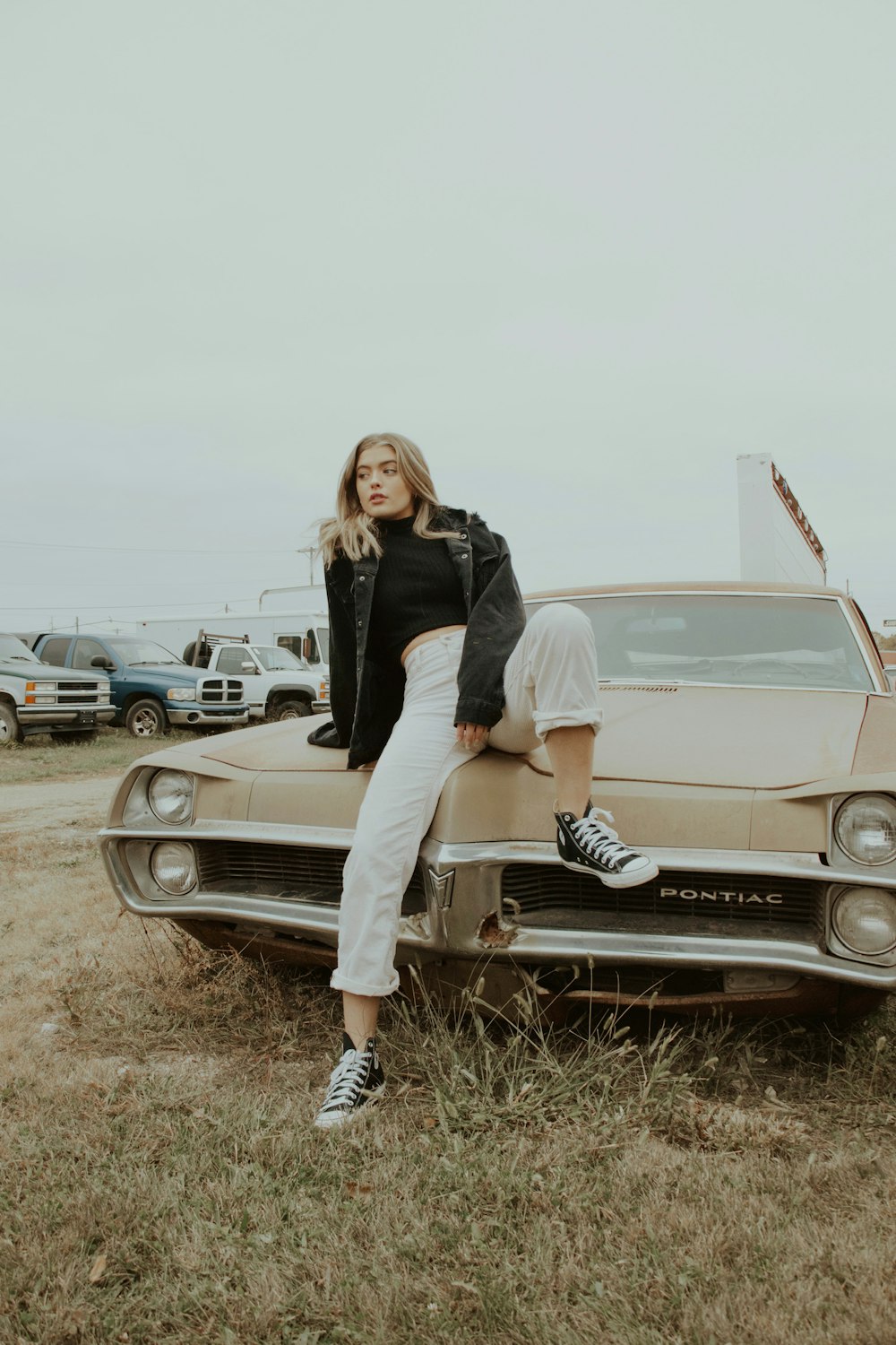 woman in black jacket and white pants sitting on white car
