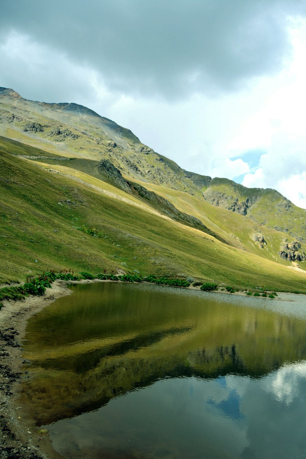 green and brown mountains beside lake under white clouds and blue sky during daytime