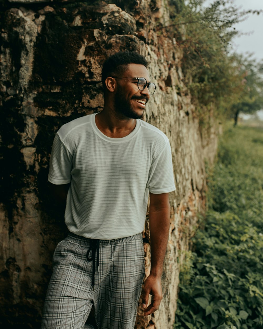 man in white crew neck t-shirt standing near brown rock