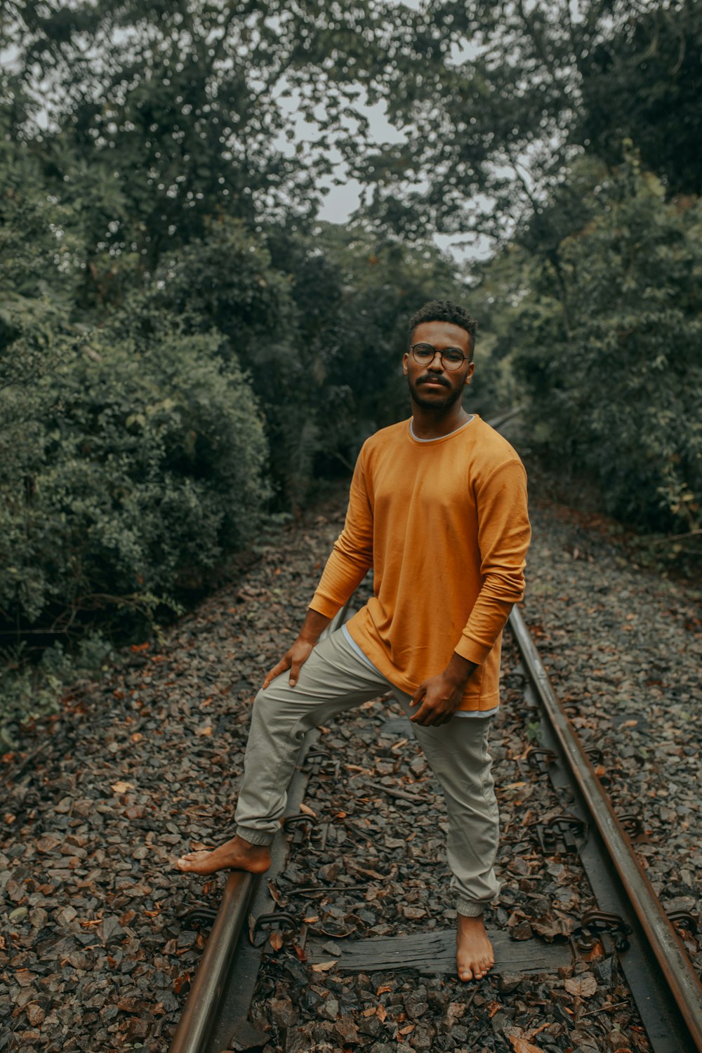 man in brown sweater and beige pants standing on train rail during daytime