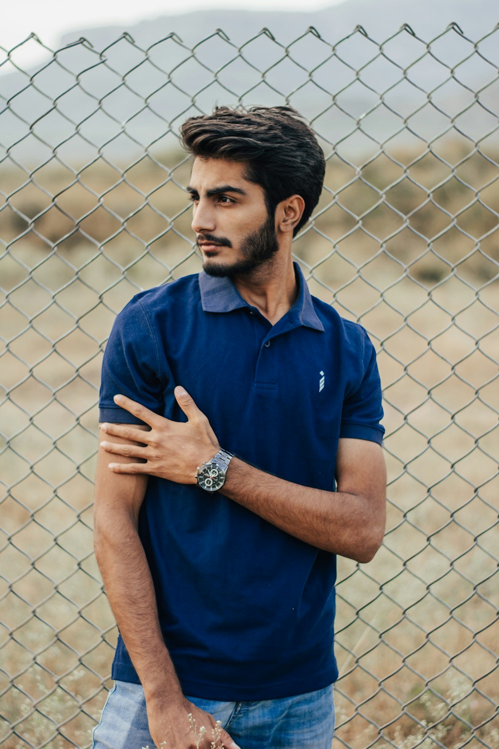 man in blue polo shirt standing near grey metal fence during daytime