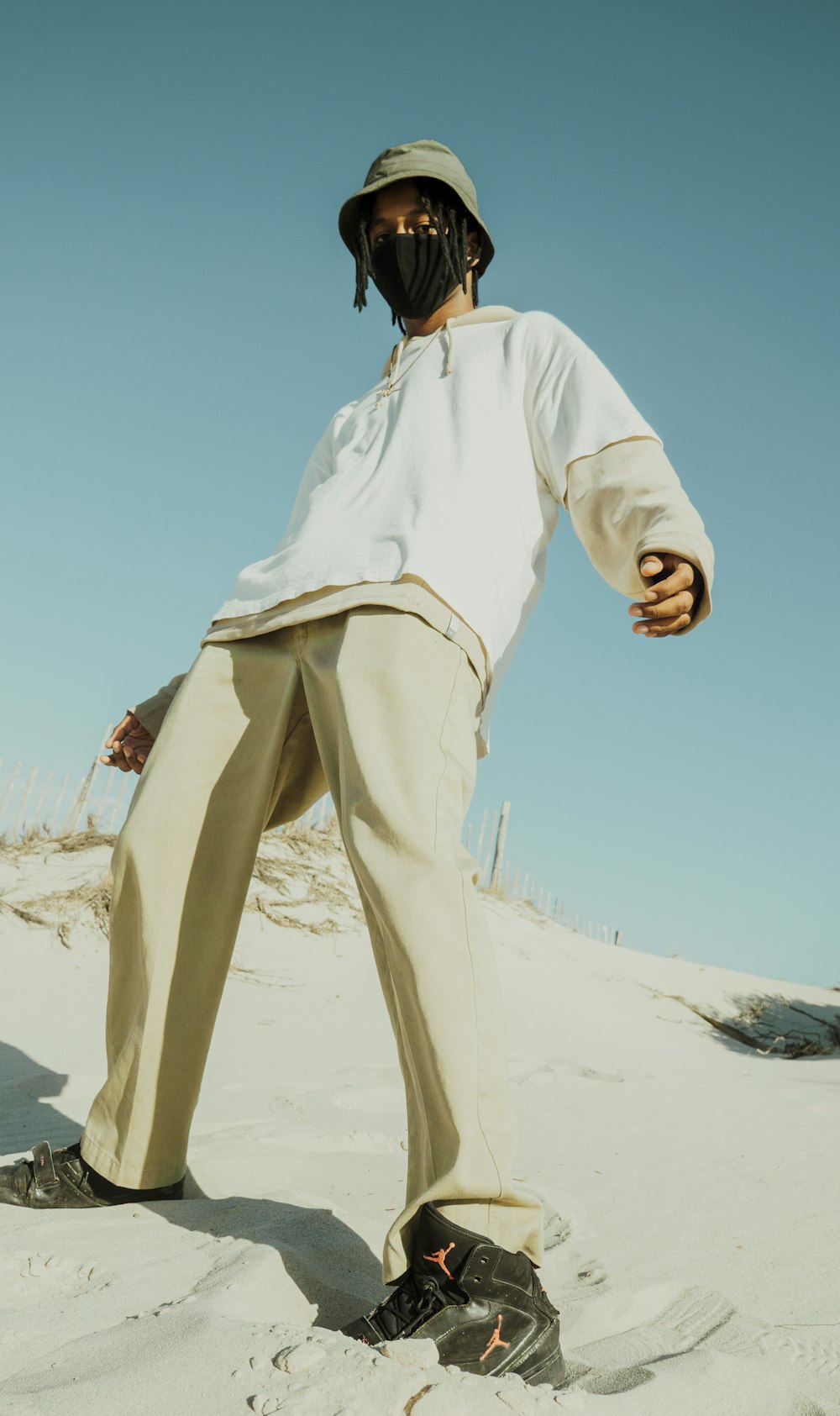 man in white long sleeve shirt and brown pants standing on white sand during daytime