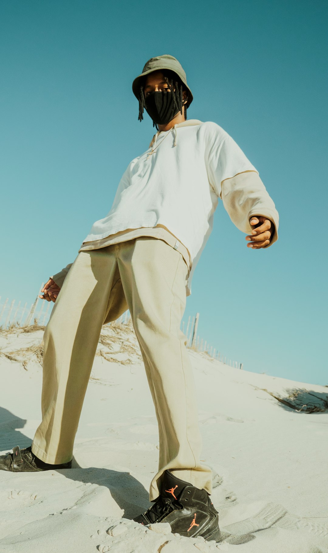 man in white long sleeve shirt and brown pants standing on white sand during daytime
