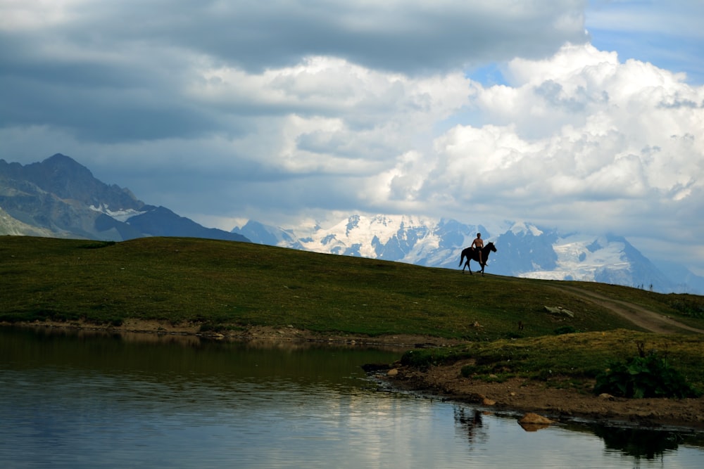 person standing on green grass field near lake under white clouds during daytime