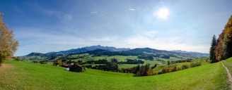 A panoramic view of a luxury farmhouse surrounded by lush green hills under a clear blue sky.