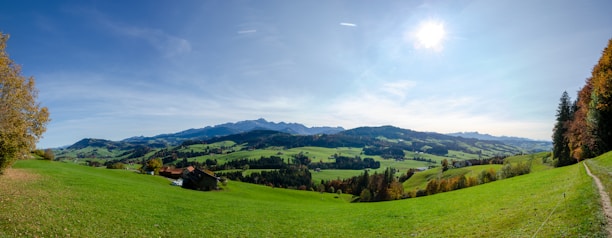A panoramic view of a luxury farmhouse surrounded by lush green hills under a clear blue sky.