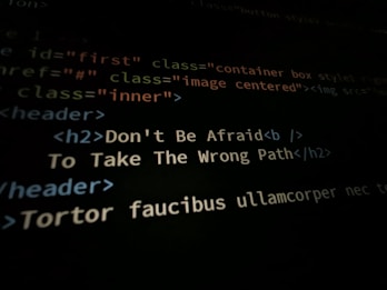 A close-up shot of a computer screen displaying HTML and CSS code. Part of the code reads 'Don't Be Afraid To Take The Wrong Path' in an h2 header tag. Other code elements using classes and tags are visible around the center message.