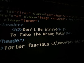 A close-up shot of a computer screen displaying HTML and CSS code. Part of the code reads 'Don't Be Afraid To Take The Wrong Path' in an h2 header tag. Other code elements using classes and tags are visible around the center message.