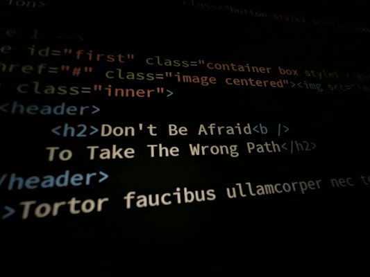 A close-up shot of a computer screen displaying HTML and CSS code. Part of the code reads 'Don't Be Afraid To Take The Wrong Path' in an h2 header tag. Other code elements using classes and tags are visible around the center message.