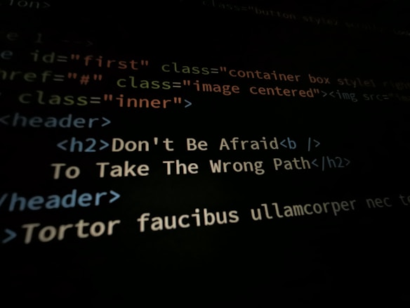 A close-up shot of a computer screen displaying HTML and CSS code. Part of the code reads 'Don't Be Afraid To Take The Wrong Path' in an h2 header tag. Other code elements using classes and tags are visible around the center message.