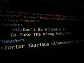 A close-up shot of a computer screen displaying HTML and CSS code. Part of the code reads 'Don't Be Afraid To Take The Wrong Path' in an h2 header tag. Other code elements using classes and tags are visible around the center message.